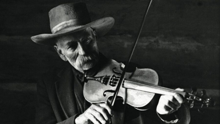 black and white image of a cowboy playing a fiddle making cowboy music